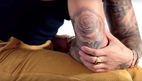 Maluma seated with tattooed arms and a rose visible on his forearm